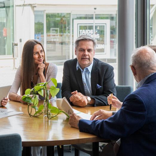 Posintralaiset istuvat pöydän ääressä keskustellen ja kuunnellen