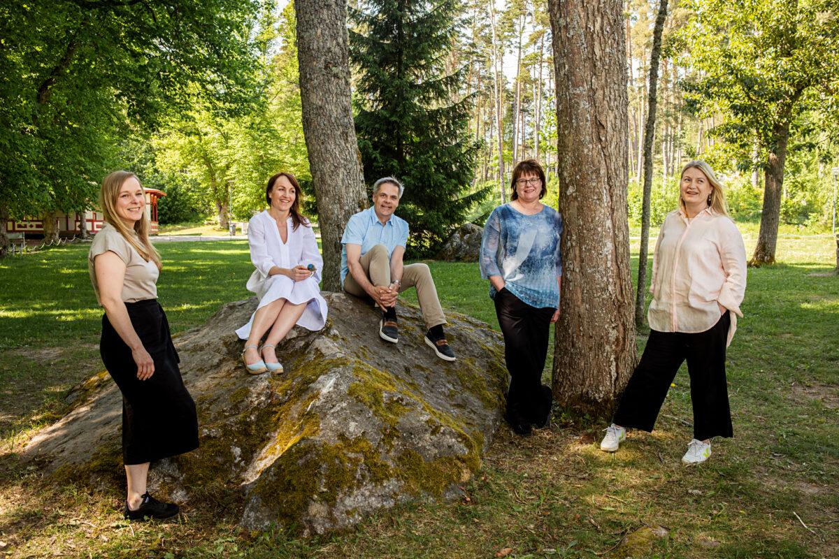 Posintran henkilöstö seisomassa ja istumassa ulkona kiven päällä.